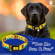 Black dog wearing a yellow 'You Me Sun & Fun' dog collar with a blurred outdoor background.