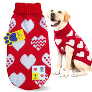 A red knit pet sweater with a white heart pattern is shown both flat on the left and worn by a light-colored dog on the right. The sweater features a ribbed red neck, a red paw print patch, and a white brand tag.