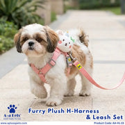 A small fluffy dog stands on a paved outdoor path wearing a pink harness and leash set with a white plush bear attachment. The photo includes A+A Pets branding and the text 'Furry Plush H-Harness & Leash Set' at the bottom.