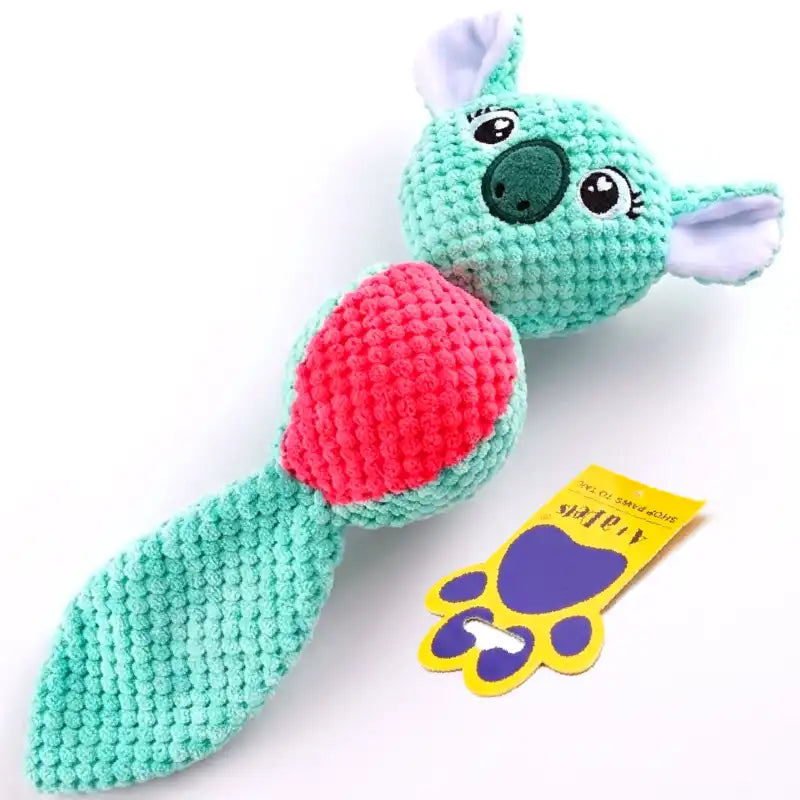 A knitted plush dog toy shaped like a koala with a pink heart-shaped belly and a long tail, shown on a white background next to a yellow and purple tag.