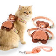 A fluffy cream-colored cat wearing a brown teddy bear harness, shown alongside the matching harness and leash laid out on a white background.