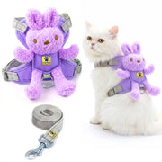 Purple plush rabbit pet harness with a matching leash, shown both empty and worn by a white cat. The harness has gray adjustable straps and a small yellow paw-print logo patch.