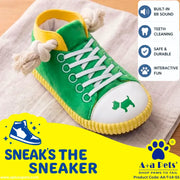 A green plush pet sneaker with white laces, a white toe cap, yellow trim, and a small green dog silhouette on the toe. The shoe is placed on a light fabric surface with promotional text and feature icons overlaid on the image.