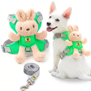 A white dog wearing a green plush dog harness with a teddy bear attachment, shown next to the harness laid out on a white background with a gray leash.