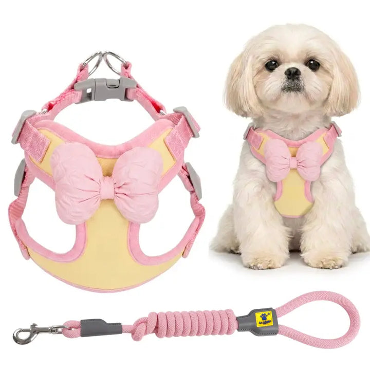 Pink and yellow pet harness with a large bow and matching leash, shown alongside a small white dog wearing the harness on a white background.