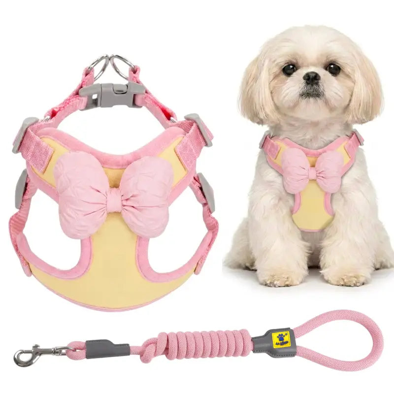 Pink and yellow pet harness with a large bow and matching leash, shown alongside a small white dog wearing the harness on a white background.