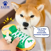 A Shiba Inu dog holds a rope tug-of-war toy in its mouth while a human hand holds a green and white sneaker-shaped dog toy in the foreground. The image features the A+A Pets brand logo in the top left and a speech bubble on the right.