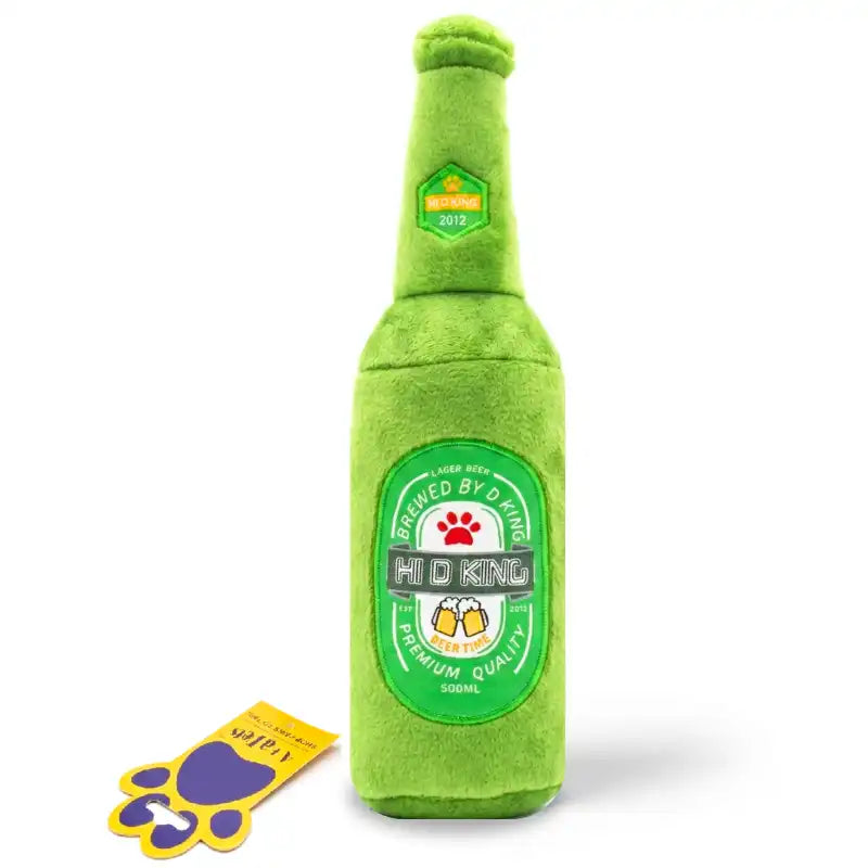 A green plush dog toy shaped like a beer bottle, featuring a circular 'Hi-D King' label design, shown on a white background with a small yellow and purple tag beside it.
