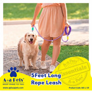 A golden retriever is being walked on a paved path outdoors while holding a purple rope leash with a blue handle. A person in a peach dress is partially visible from the waist down.