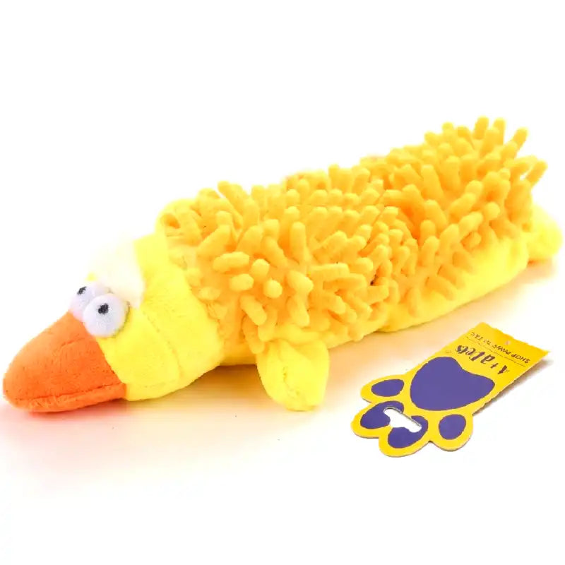 A yellow plush duck toy with a fuzzy, chenille-like body, an orange beak, and white eyes, shown on a white background with a small yellow-and-purple tag beside it.