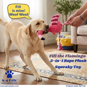 A yellow Labrador retriever plays with a pink flamingo-shaped rope plush toy in a living room. A human hand is holding the other end of the toy.