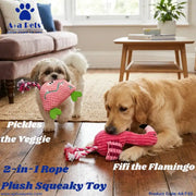 Two dogs in a living room setting demonstrating a pink 2-in-1 plush squeaky rope toy. One dog holds the toy shaped like a green vegetable with a pink face, and the other dog chews the pink flamingo-shaped end of the rope toy.